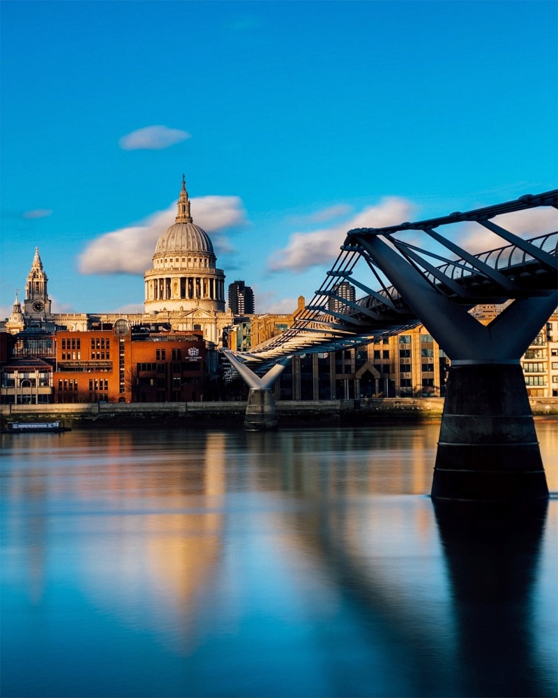 St Paul's Cathedral in London, England on a magnificent sunny day with the millennium bridge in the foreground spanning the river Thames.